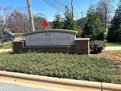 A sign for Cambridge Oaks II Apartments is displayed in front of a hedge.