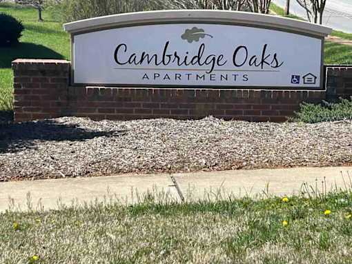 A sign for Cambridge Oaks Apartments is displayed in front of a grassy area.