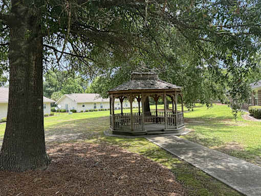 A gazebo sits in the middle of a grassy area with a tree in the foreground.