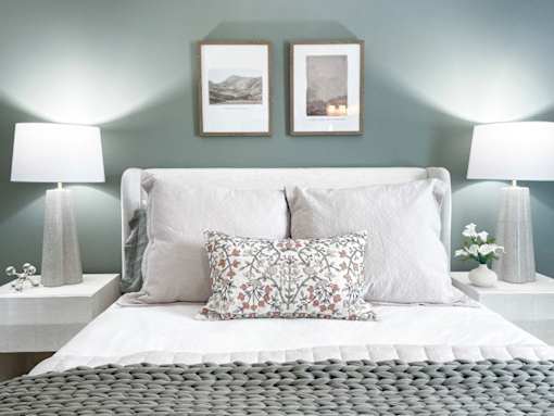 A bed with a white comforter and two decorative pillows sits in a room with two lamps on each side.