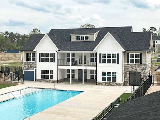 A large white house with a black roof and a pool in front.