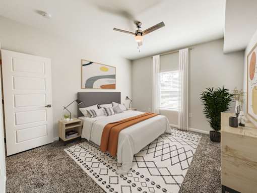 Northbrook Apartments carpeted bedroom, staged with a full-sized bed, side tables, paintings and a house plant.