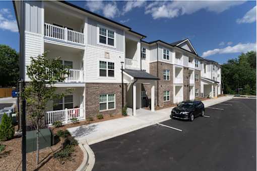 A black car is parked in a parking lot in front of a white apartment building.