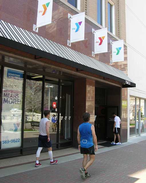 Two men are walking past a YMCA building.