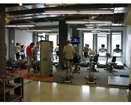A gym with people exercising and a TV screen on the wall.