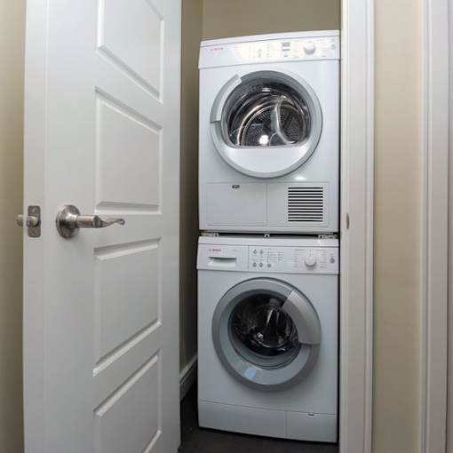 A white door is open to a small laundry room with a washer and dryer stacked on top of each other.