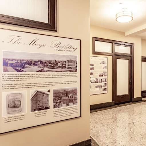A wall with a framed poster titled "The Mayo Building" with a panoramic view of Boston Associates in 1930 and other historical facts.
