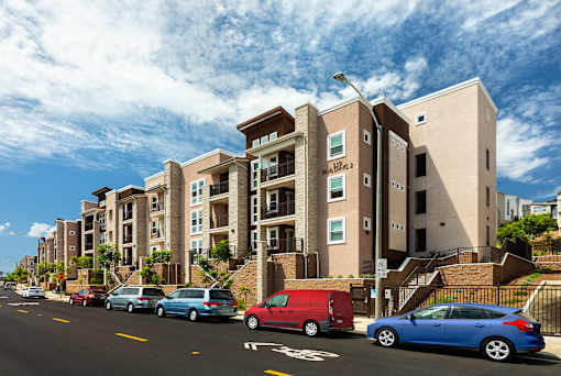 Cars are parked on the side of the road in front of apartment buildings.