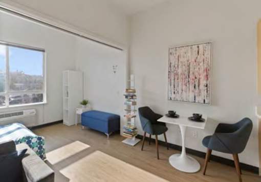 A living room with a blue ottoman, a white table, and a painting on the wall.