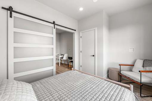 A bedroom with a bed, a chair, a couch, and a sliding door.