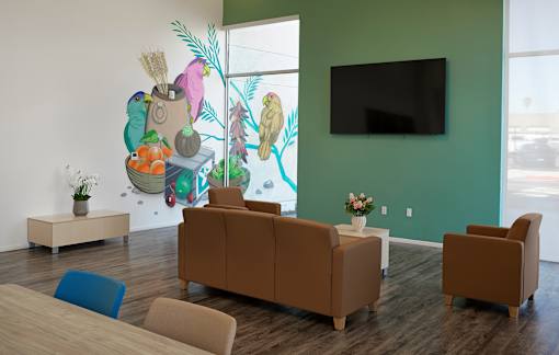 A living room with a brown couch and a green wall with a mural of a bear and a tree.