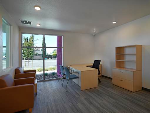 A room with a desk, chairs, and a window overlooking a parking lot.