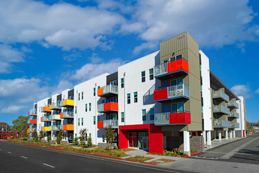 A modern multi-story apartment building with balconies and a mix of red, yellow, and white colors.
