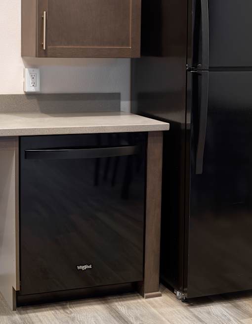A black refrigerator stands next to a black drawer in a kitchen.
