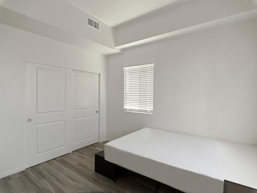 A white bedroom with a bed, dresser, and window.
