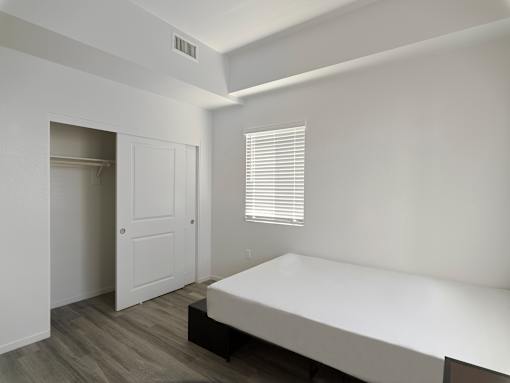 A white bedroom with a bed, dresser, and window.