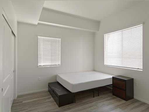 A bedroom with a bed, nightstand, and window with blinds.