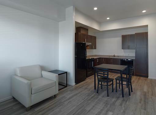 A kitchen with a black refrigerator, a table with two chairs, and a white chair.