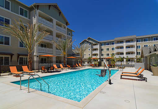A swimming pool surrounded by orange lounge chairs and palm trees.