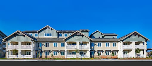 A large, modern apartment building with multiple balconies and a mix of grey and white exterior.