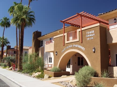 A building with a sign that says "Cedar Village Apartments" in front of some palm trees.