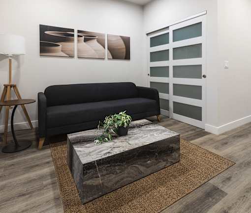 A black couch sits in a room with a grey wall and a brown rug.
