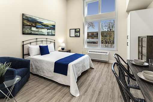 A bedroom with a bed, a chair, a table, and a painting on the wall.