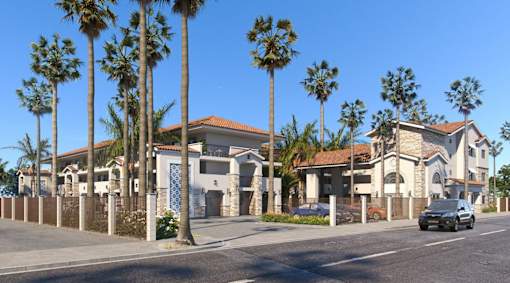 A row of palm trees line a street in front of a row of houses.
