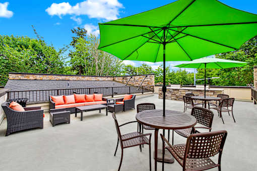 A patio with a green umbrella and brown furniture.