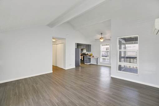 A room with a ceiling fan and a kitchenette in the background.