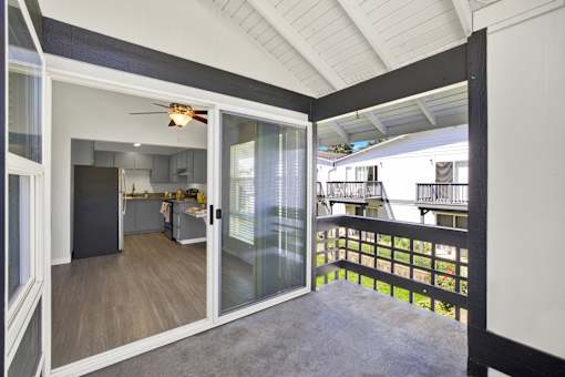 A balcony with a glass railing and sliding glass doors leading to a kitchen.
