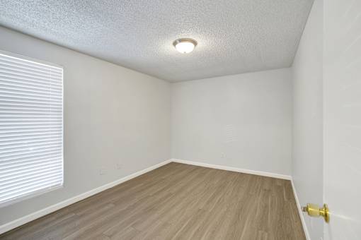 A room with a wooden floor and a window with blinds.