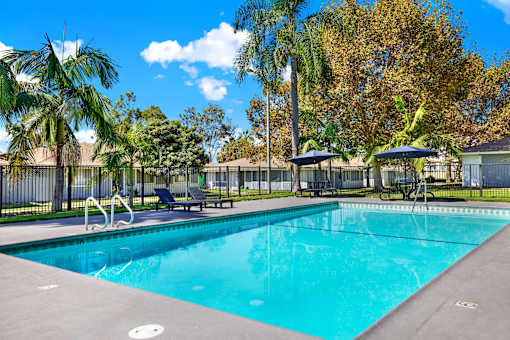 Outdoor swimming pool with lounge chairs and umbrellas at Coventry Square Apartments, Upland, California