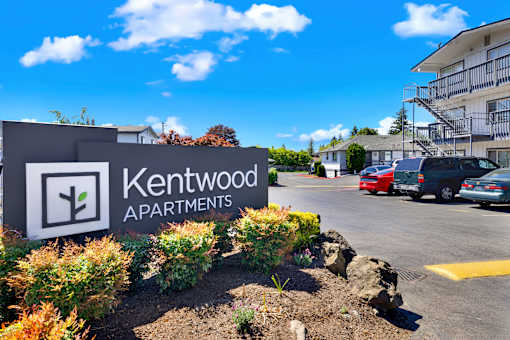 A sign for Kentwood Apartments is in front of a parking lot.