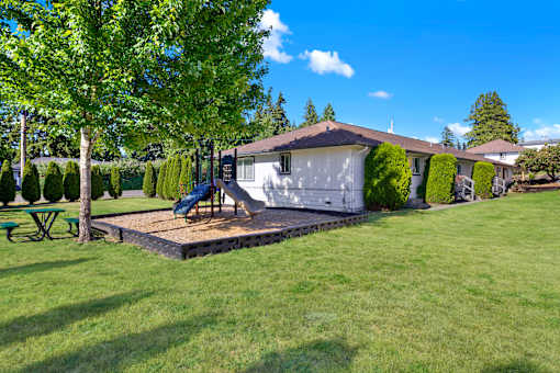 A house with a green lawn and a slide in the backyard.