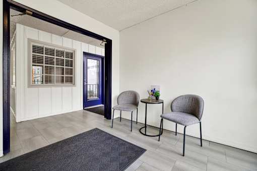 Two grey chairs are placed in front of a white wall.