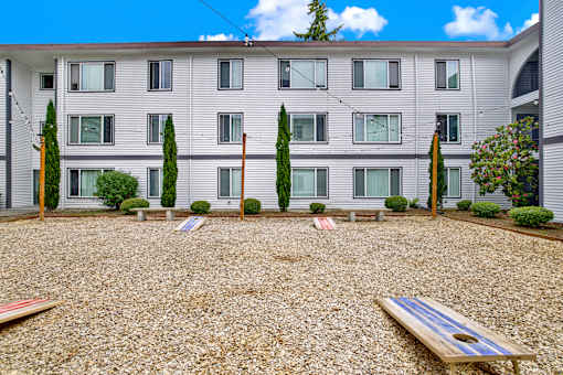 A building with a grey facade and a gravel yard with a bench.