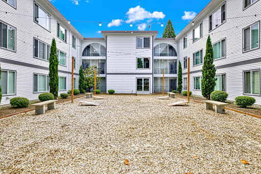 A courtyard surrounded by apartment buildings with a gravel ground and trees.