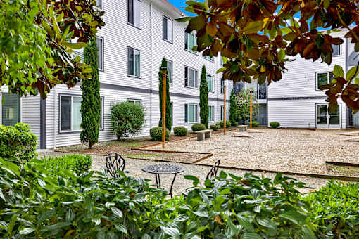 A white building with a gravel courtyard and a tree with a brown trunk.