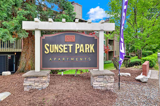 A sign for Sunset Park Apartments is displayed in front of a building.