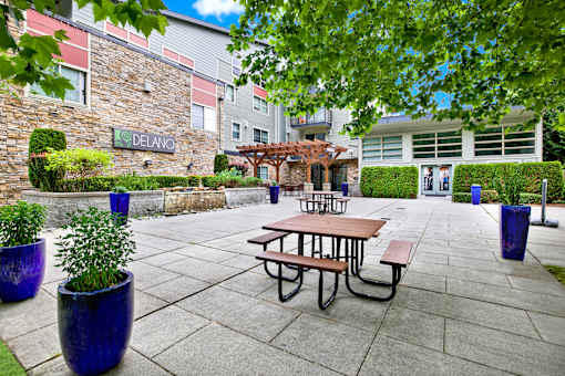 A Delano sign is on a building behind a small garden area.