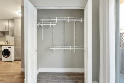 A white laundry room with a dryer and a white closet with shelves.at Federal Apartments, Los Angeles, CA 90025
