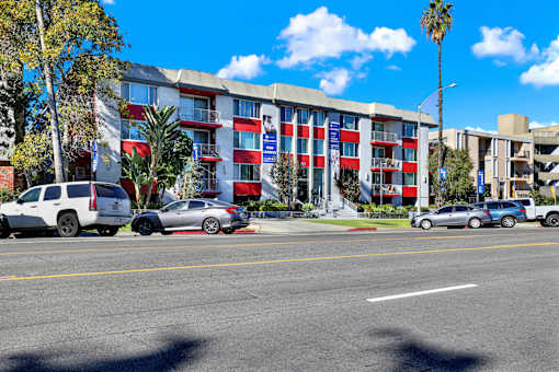 A multi-story building with a red, white, and blue color scheme is surrounded by parked cars and palm trees. at Chateau La Fayette, Los Angeles, CA, 90057