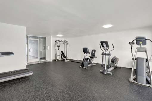 A spacious gym with a variety of equipment including treadmills, stationary bikes, and weight machines. at Chateau La Fayette, California