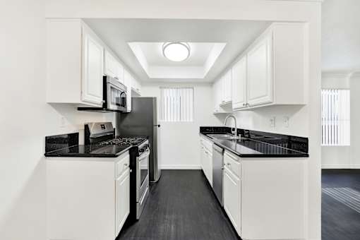 A modern kitchen with white cabinets and black countertops. at Elmwood Gardens, Burbank, CA, 91502
