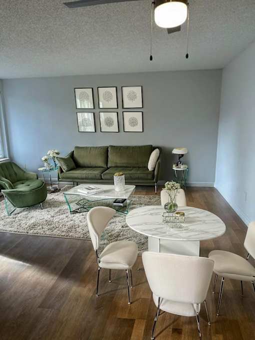 A living room with a green couch, white chairs, and a glass table.