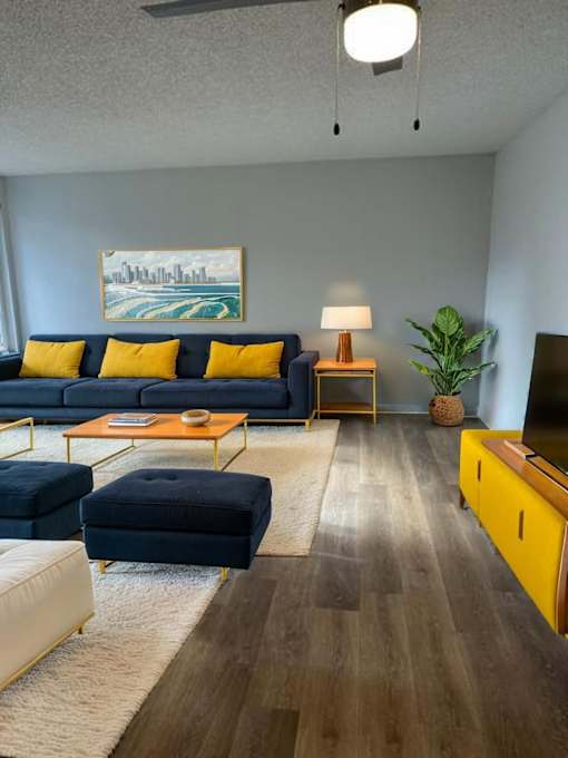 A living room with a blue couch, yellow pillows, and a painting on the wall.
