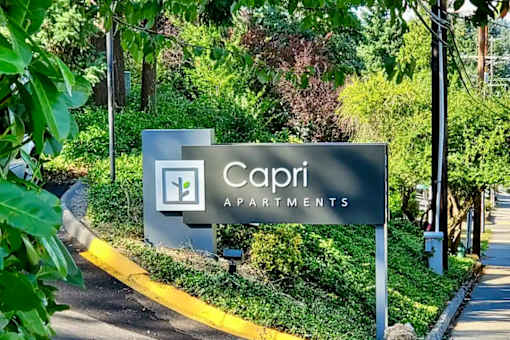 A sign for Capri Apartments is shown in front of a green landscape.