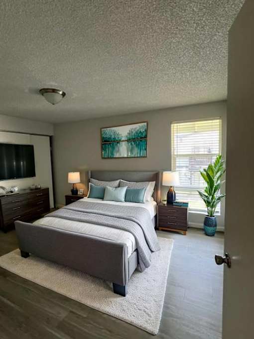A bedroom with a large bed, a nightstand with a lamp, and a painting on the wall.