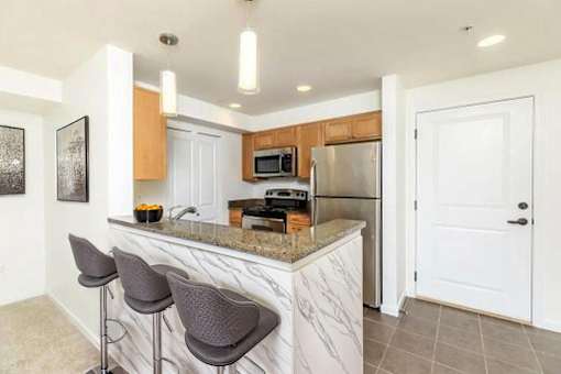 A kitchen with a marble countertop and bar stools.
